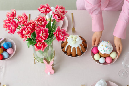 Female hands decorating festive table setting with painted eggs and Easter cake. Closeup