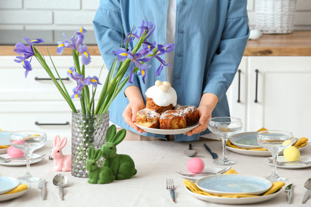 Woman putting plate with Easter cakes on table setting for Easter celebration in kitchen. Closeup