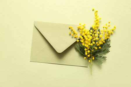 Envelope with beautiful yellow mimosa flowers on green background