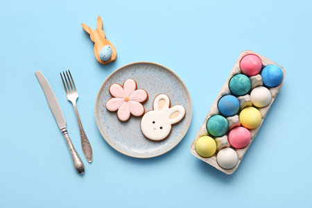 Beautiful table setting with sweet cookies and Easter eggs on blue background