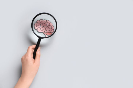 Female hand with magnifying glass and paper human brain on gray background. Cancer concept