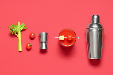 Glass of bloody mary with celery, tomatoes, measuring cup and shaker on red backgroundの写真素材