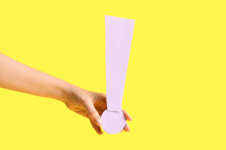 Female hand with paper exclamation mark on yellow background, closeup