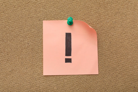 Pink sticky note with exclamation mark pinned on boardの写真素材