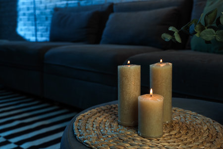 Burning candles on pouf in dark living room, closeupの写真素材