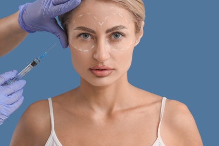 Young woman with marks on her face receiving injection against blue background, closeup....