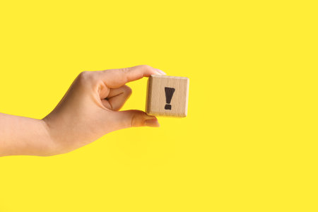 Woman holding wooden cube with exclamation mark on yellow background, closeupの写真素材