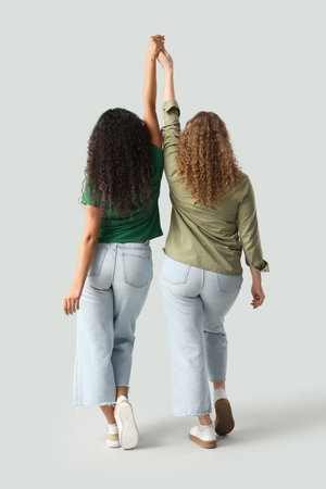 Young women holding hands on light background, back view.の写真素材
