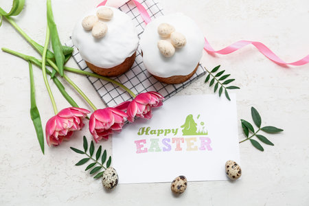 Sweet Easter cakes with eggs, greeting card and beautiful tulip flowers on white backgroundの写真素材