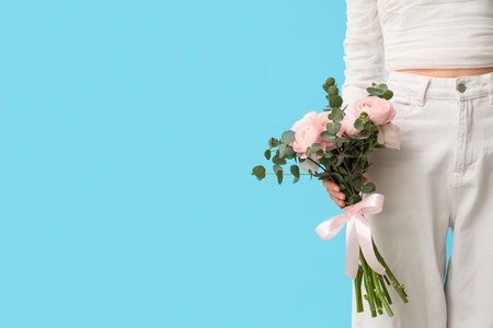 Young woman with bouquet of ranunculus flowers and eucalyptus on blue backgroundの写真素材
