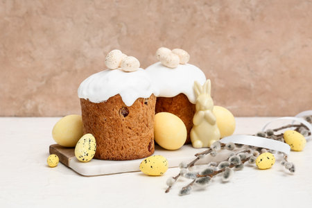 Sweet Easter cakes with yellow eggs, toy rabbit and willow branches on white table