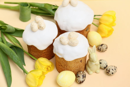 Sweet Easter cakes with eggs, toy rabbit and beautiful tulip flowers on yellow background