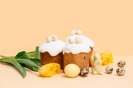 Sweet Easter cakes with eggs, toy rabbit and beautiful tulip flowers on yellow background