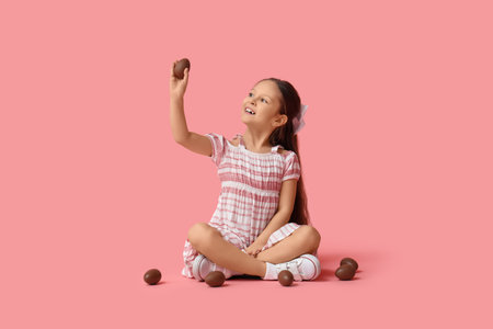 Cute little girl with sweet chocolate eggs sitting on pink background. Easter celebrationの写真素材