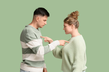 Young couple pointing to each other while quarreling on green backgroundの写真素材