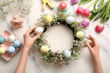 Woman making Easter wreath with flowers and painted eggs on marble backgroundの写真素材