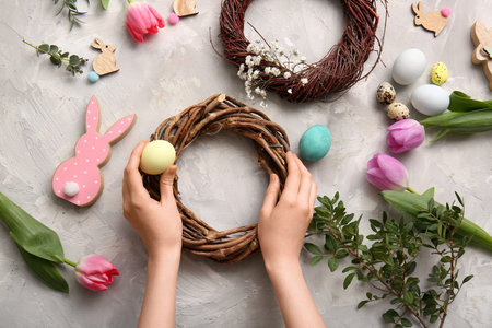 Woman decorating Easter wreath with flowers, branches and painted eggs on gray grunge background