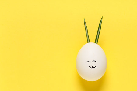 Funny Easter egg with drawn face and bunny ears on yellow backgroundの写真素材