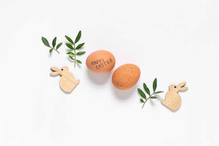 Composition with Easter eggs, wooden bunnies and plant leaves on light backgroundの写真素材