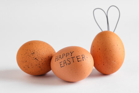 Chicken eggs with text HAPPY EASTER and bunny ears on light backgroundの写真素材
