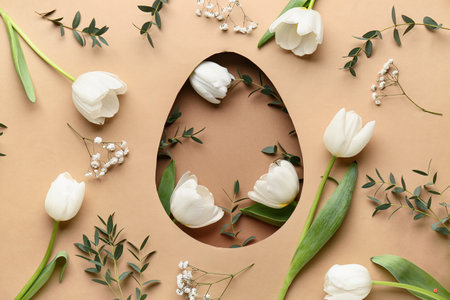 Easter composition with flowers and green leaves visible through egg-shaped hole on beige backgroundの写真素材