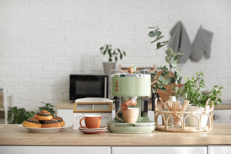 Modern coffee machine, cups and buns on table in kitchenの写真素材
