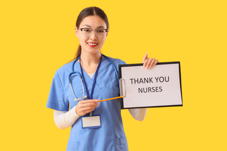 Female Asian doctor holding clipboard with text THANK YOU NURSES on yellow backgroundの写真素材