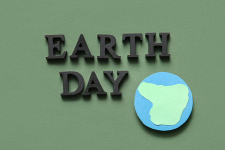 Text EARTH DAY with paper planet on green background