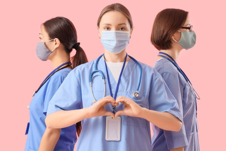 Female doctors in medical masks making heart gesture on pink background. International Nurses Dayの写真素材