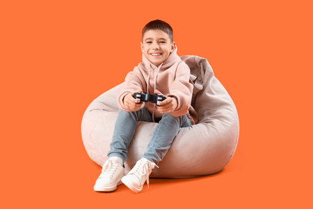 Little boy playing video game on beanbag against orange background