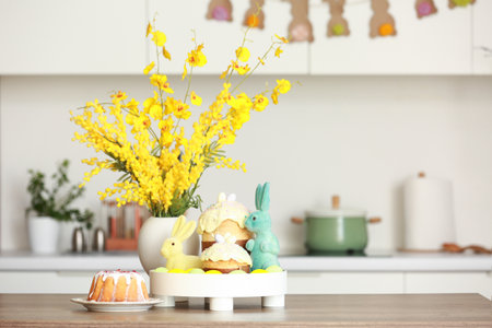 Vase with mimosa flowers, Easter rabbits and cakes on table in kitchenの写真素材