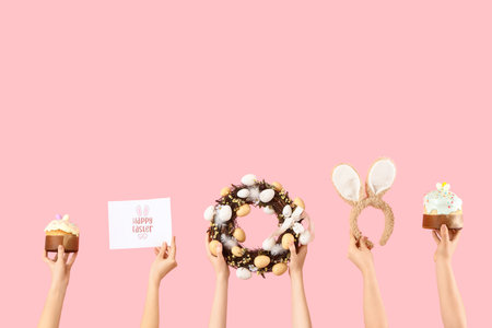 Female hands with Easter cakes, card, wreath and bunny ears on pink backgroundの写真素材