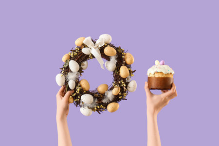 Female hands with Easter wreath and cake on lilac background