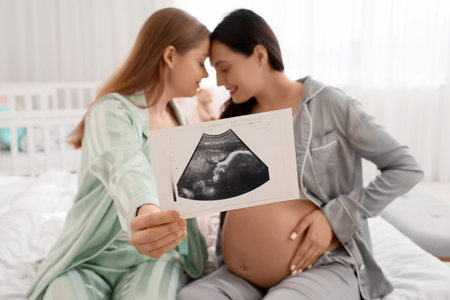 Young pregnant lesbian couple with sonogram image in bedroom, closeupの写真素材