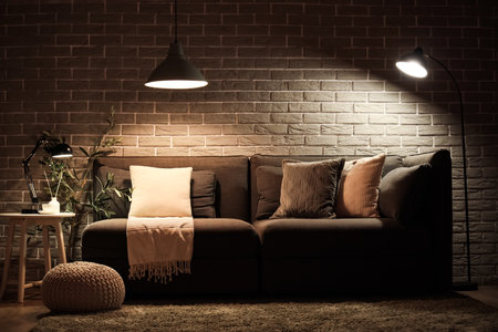 Stylish interior of living room with comfortable sofa, pouf and glowing lampsの写真素材