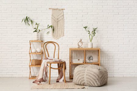 Wooden chair, stylish pouf, shelving units with bamboo stems and decor near light brick wall