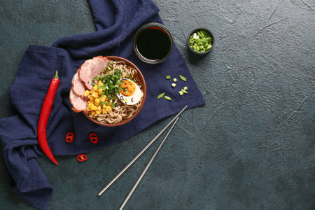 Bowl of ramen noodle soup with meat and canned corn seeds on dark backgroundの写真素材