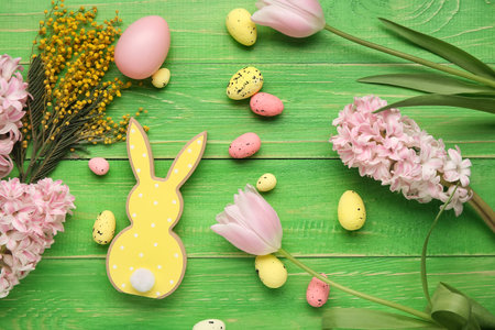 Composition with Easter eggs, decorative rabbit and flowers on green wooden background