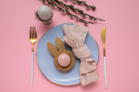 Beautiful table setting with Easter eggs and willow branches on pink background