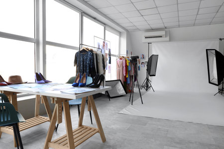 Interior of stylish photo studio with professional equipment, table and clothes racks