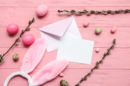 Envelope with blank card, Easter eggs, bunny ears and willow branches on pink wooden backgroundの写真素材