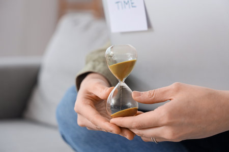 Woman with hourglass and laptop at home, closeupの写真素材