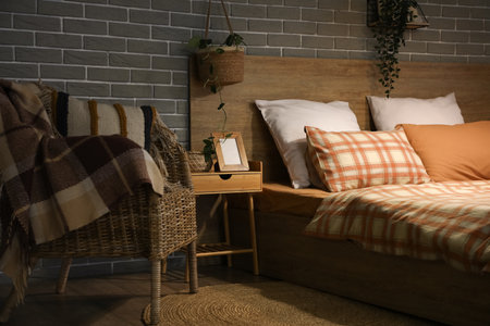 Big comfortable bed and table with photo frame in room at nightの写真素材