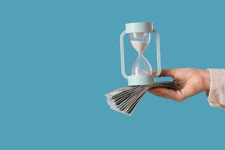 Woman holding hourglass with money on blue background