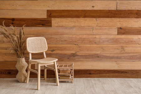 Comfortable chair with vase of pampas grass and books near wooden wallの写真素材