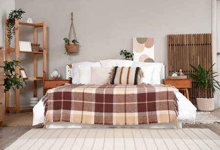 Bedside table, large comfortable bed and folding screen in interior of light bedroom