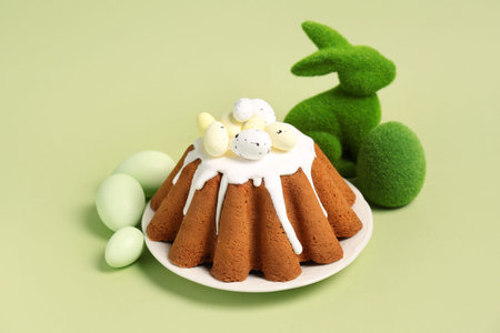 Plate of sweet Easter bread with eggs and toy rabbit on green background