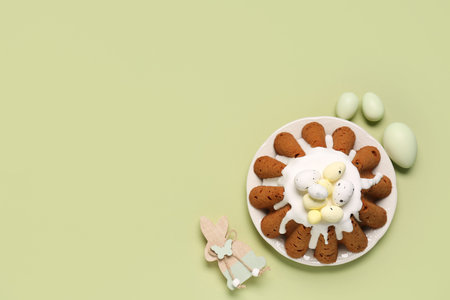 Plate of sweet Easter bread with eggs and wooden rabbit on green background