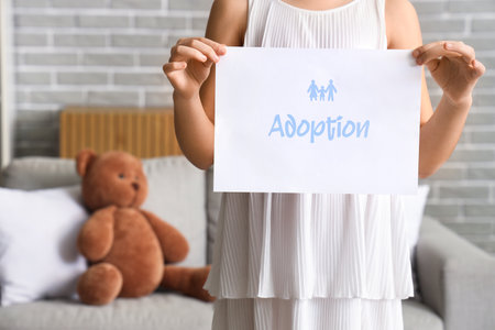 Girl holding paper with word ADOPTION at home, closeupの写真素材