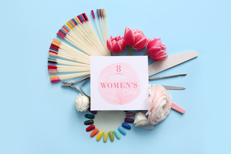 Manicure instruments with artificial nails palettes and beautiful flowers on blue background. International Women's Day celebrationの写真素材